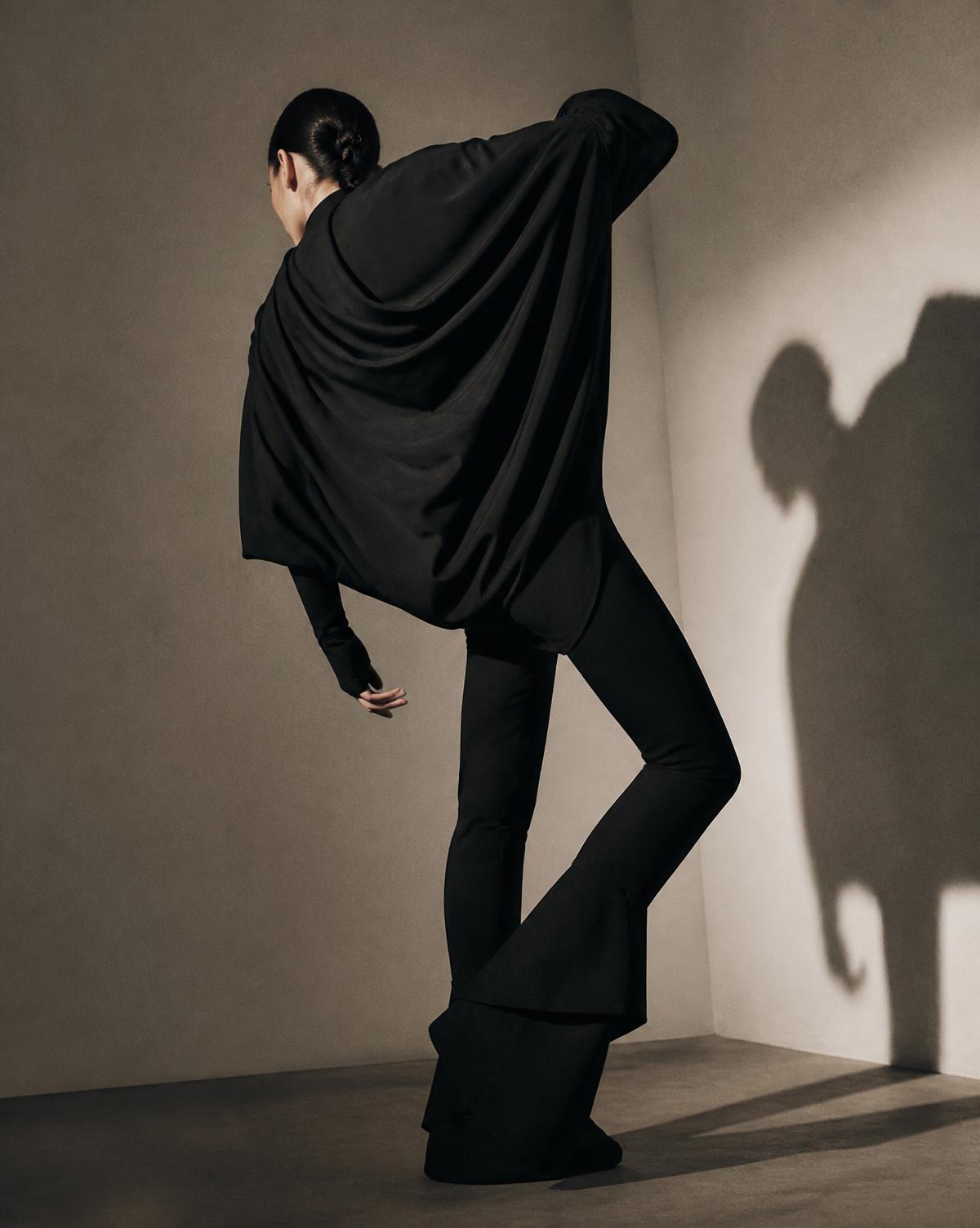 A model in an exaggerated draped black activewear silhouette