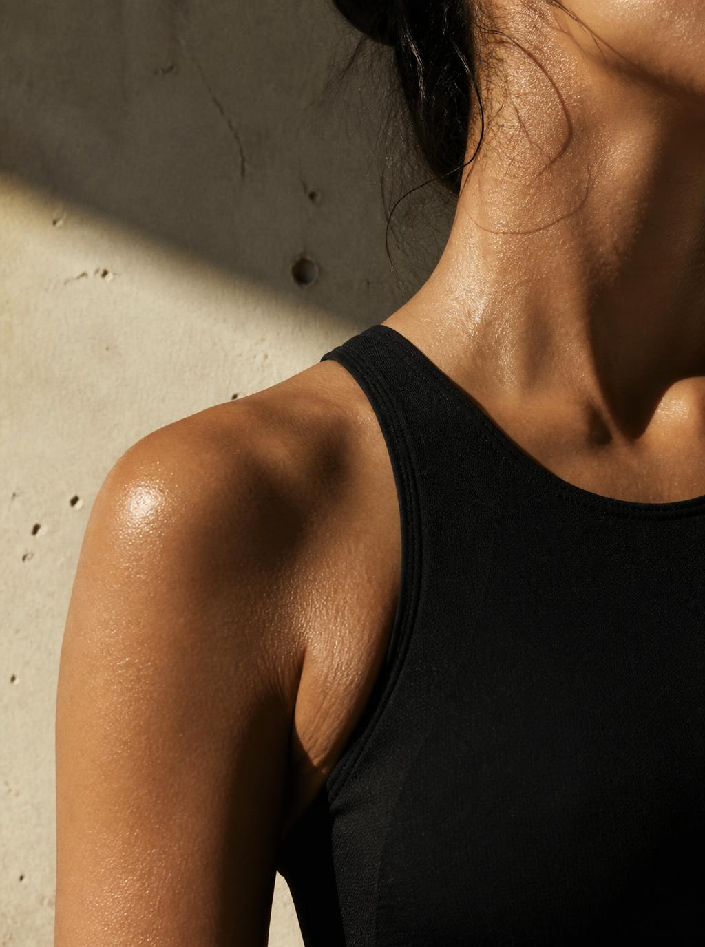 Close-up of a sweat-lit shoulder in a black Paseena tank against concrete