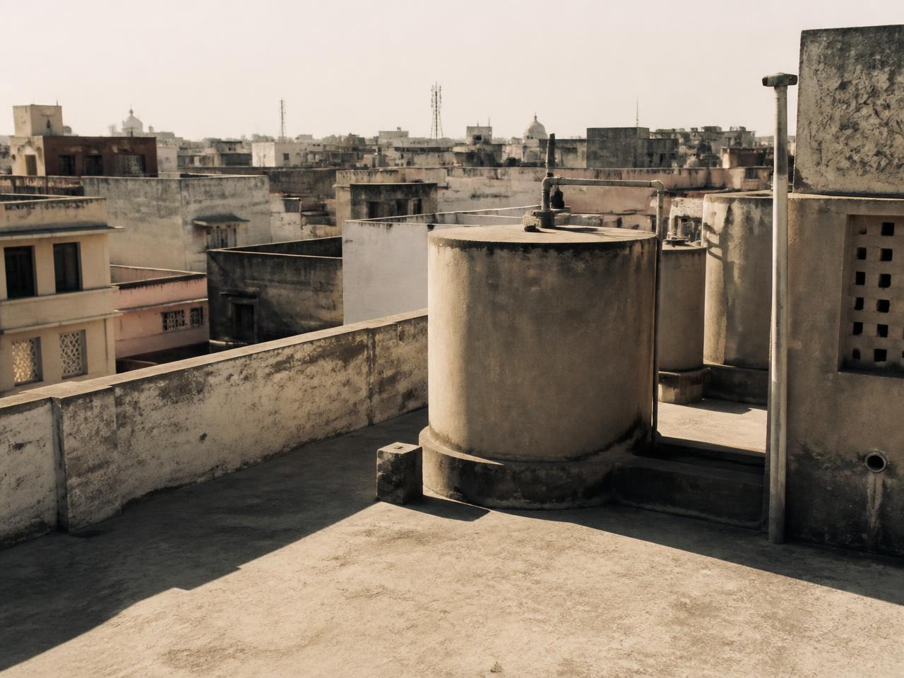 Sunlit rooftop water tanks over a dense Indian city in summer